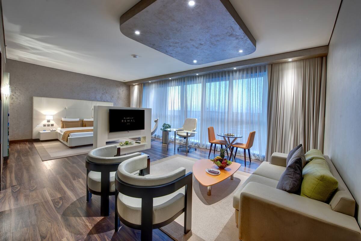 A modern hotel room with a large bed, a TV, a seating area with a coffee table, and a dining table with chairs.