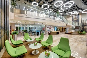 Um hall moderno com cadeiras verdes, uma escada e um balcão de recepção.