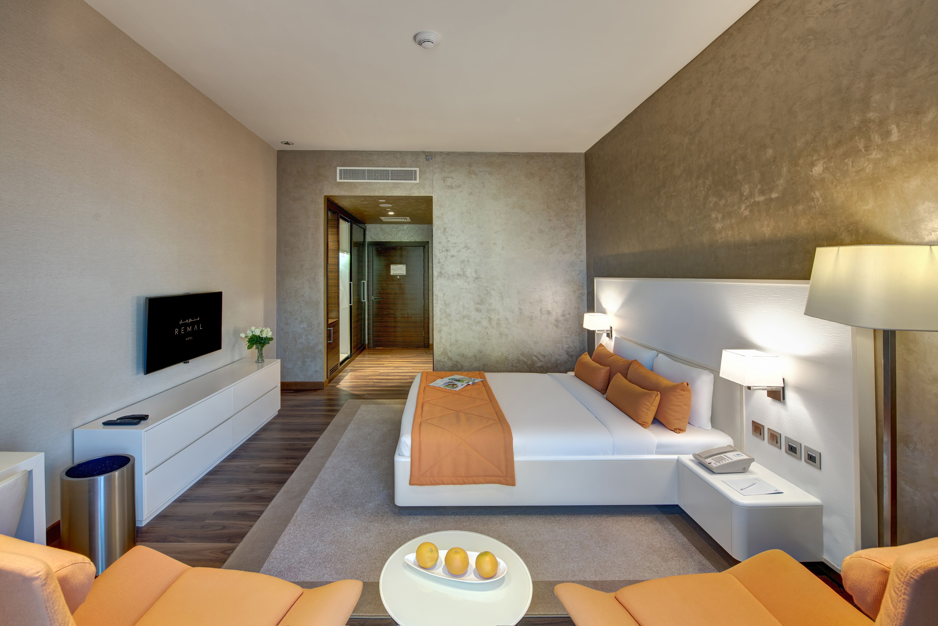 A modern hotel room with a large bed, bedside tables, a TV, and a seating area with a table and chairs.