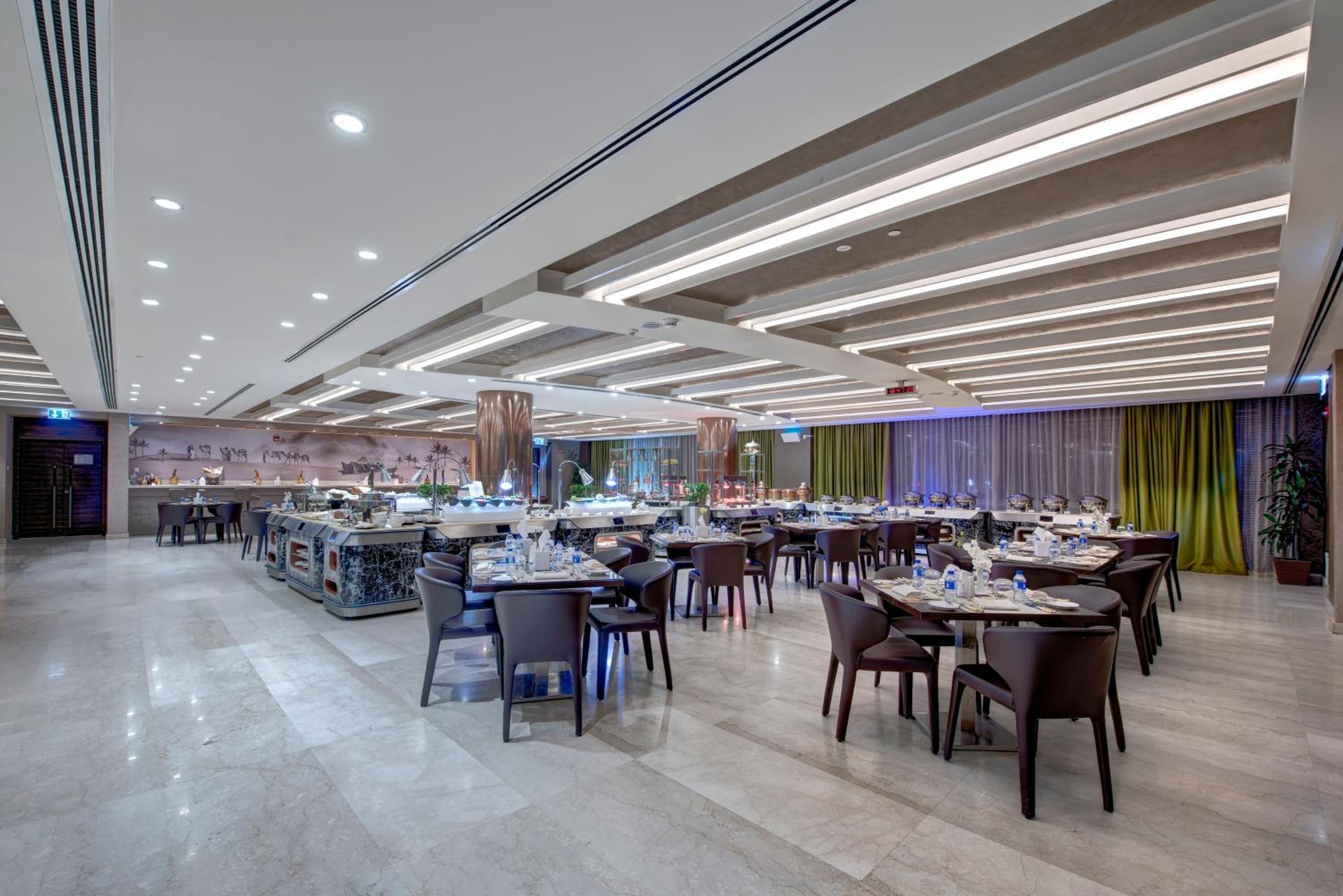 A spacious restaurant with a modern ceiling design, marble flooring, and a variety of seating arrangements.