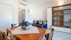 Un comedor con una mesa de madera, sillas y un centro de mesa floral. En el fondo, un sofá azul con cojines estampados.