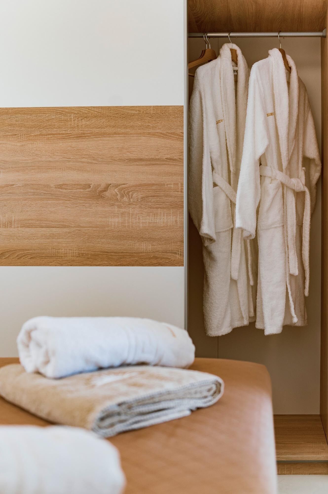 Ein hölzerner Kopfseitenverkleidung, eine Holzbank mit gefalteten Handtüchern und ein Holzschrank mit zwei weißen Bademänteln.