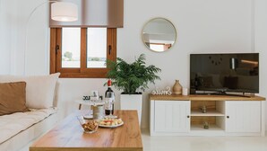 Ett vardagsrum med en soffa, ett soffbord med snacks, en tv, en krukväxt och en spegel.