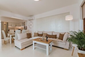 Un salon moderne avec un canapé d’angle, une table basse et un coin repas avec des chaises.