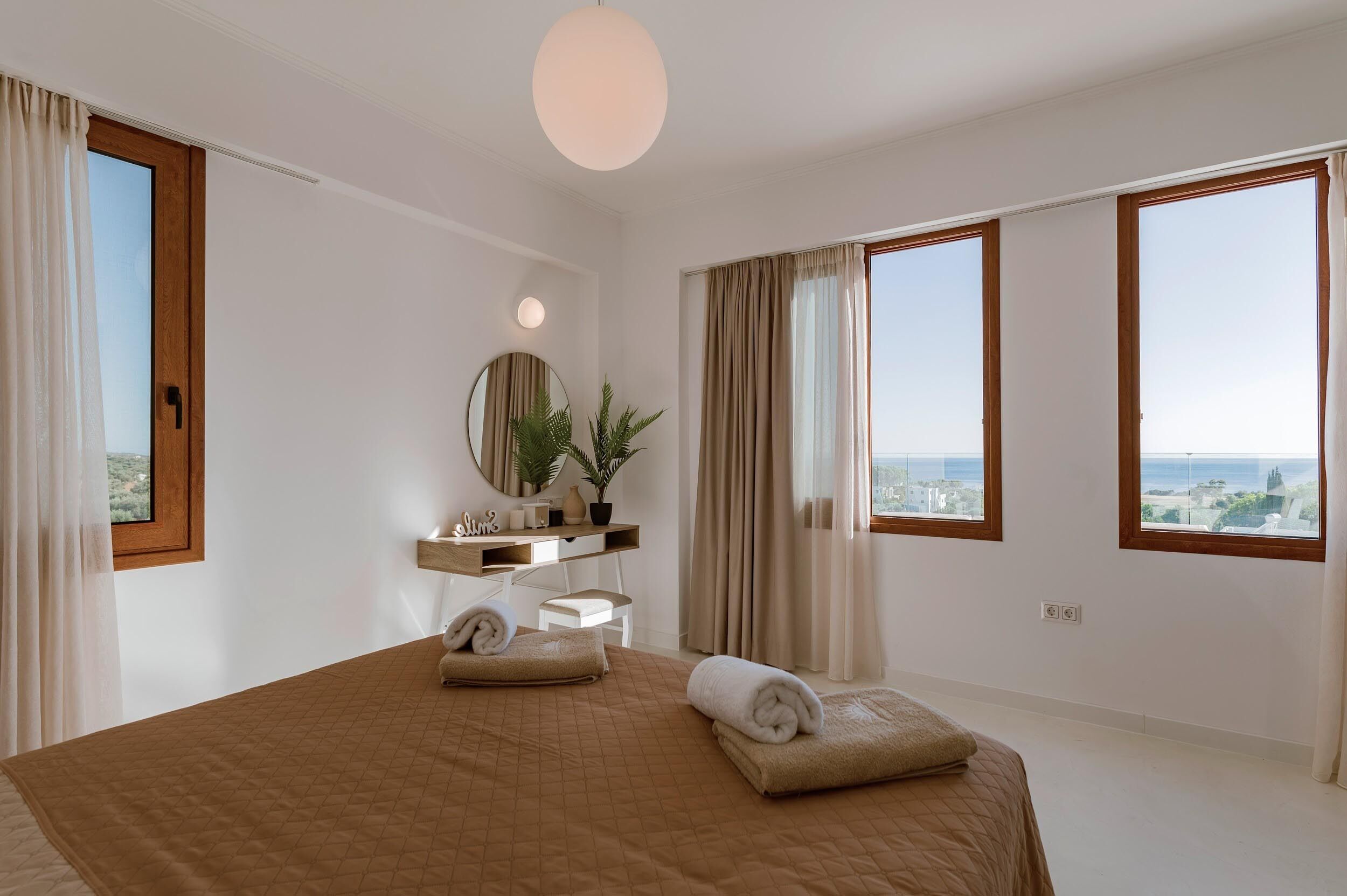 Ein Schlafzimmer mit einem großen Bett, einem Nachttisch, einem Spiegel, einer Zimmerpflanze und Blick auf die Stadt.
