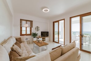 Un salon moderne avec un canapé, une table basse, un téléviseur et un balcon aménagé avec du mobilier d’extérieur.