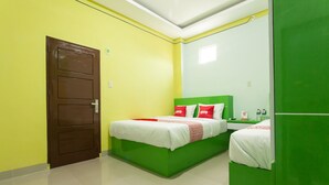 A room with two beds, a green headboard, and a white wall.