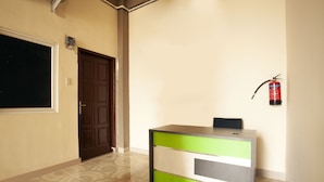 A reception desk with a green and grey color scheme, a fire extinguisher mounted on the wall, and a door with a brown frame.
