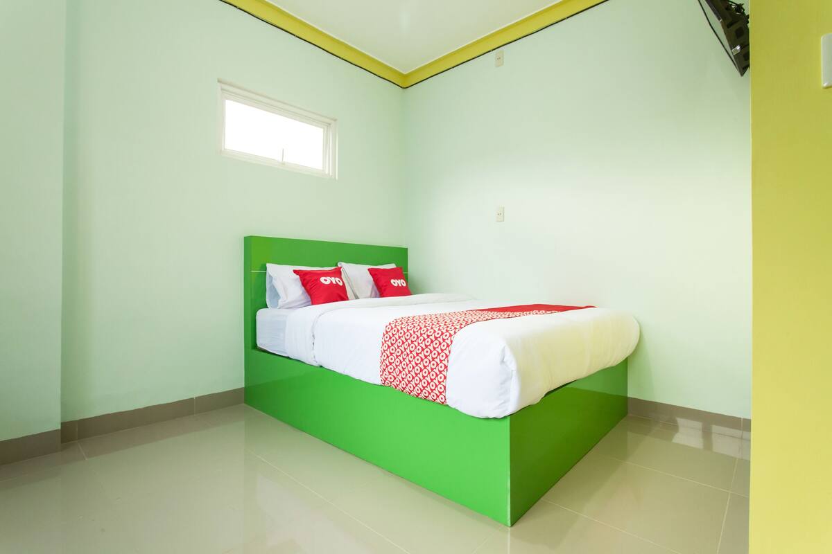 Une chambre avec un lit vert, du linge de lit blanc et des oreillers rouges.