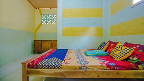A room with a wooden bed, colorful bedding, a small wooden cabinet, and a window with a decorative screen.