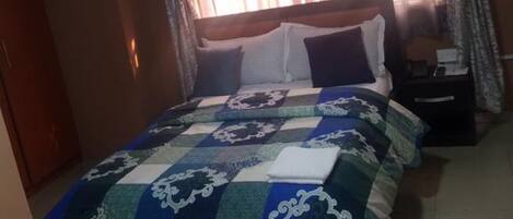 A bedroom with a large bed, a nightstand, and a window with curtains.
