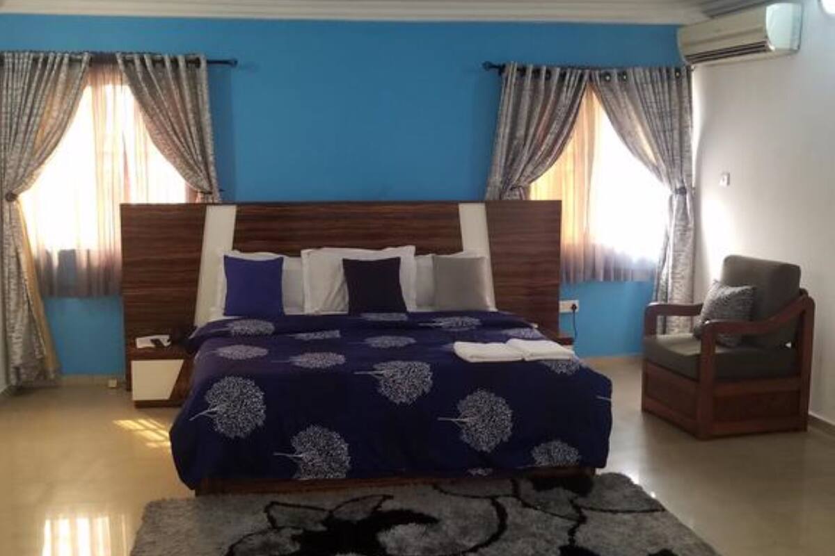 A bedroom with a large bed, a wooden headboard, a chair, and curtains.