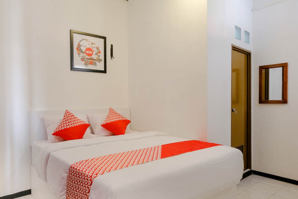 Une chambre à coucher avec un lit, deux oreillers, un tableau encadré au mur et une porte.
