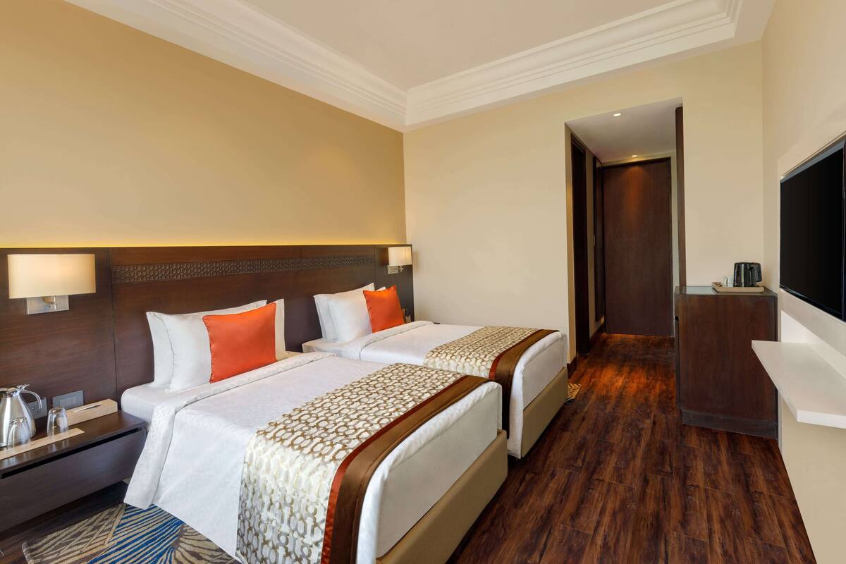 Een hotelkamer met twee bedden, een bureau, een televisie en een houten vloer.