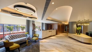 A modern lobby with a reception desk, seating area, and large windows. - Ginger Greater Noida Pari Chowk (Greater Noida)