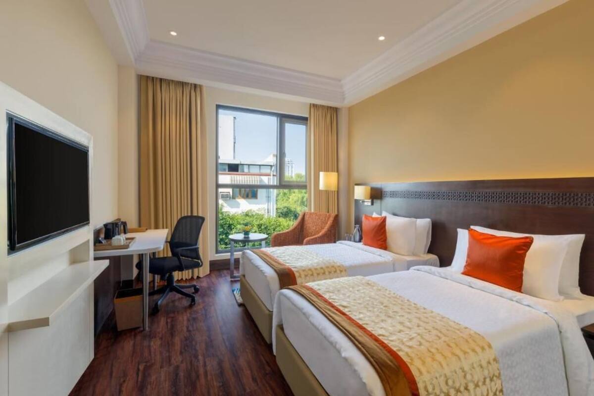 Een hotelkamer met twee bedden, een bureau, een stoel, een televisie en een raam met gordijnen.