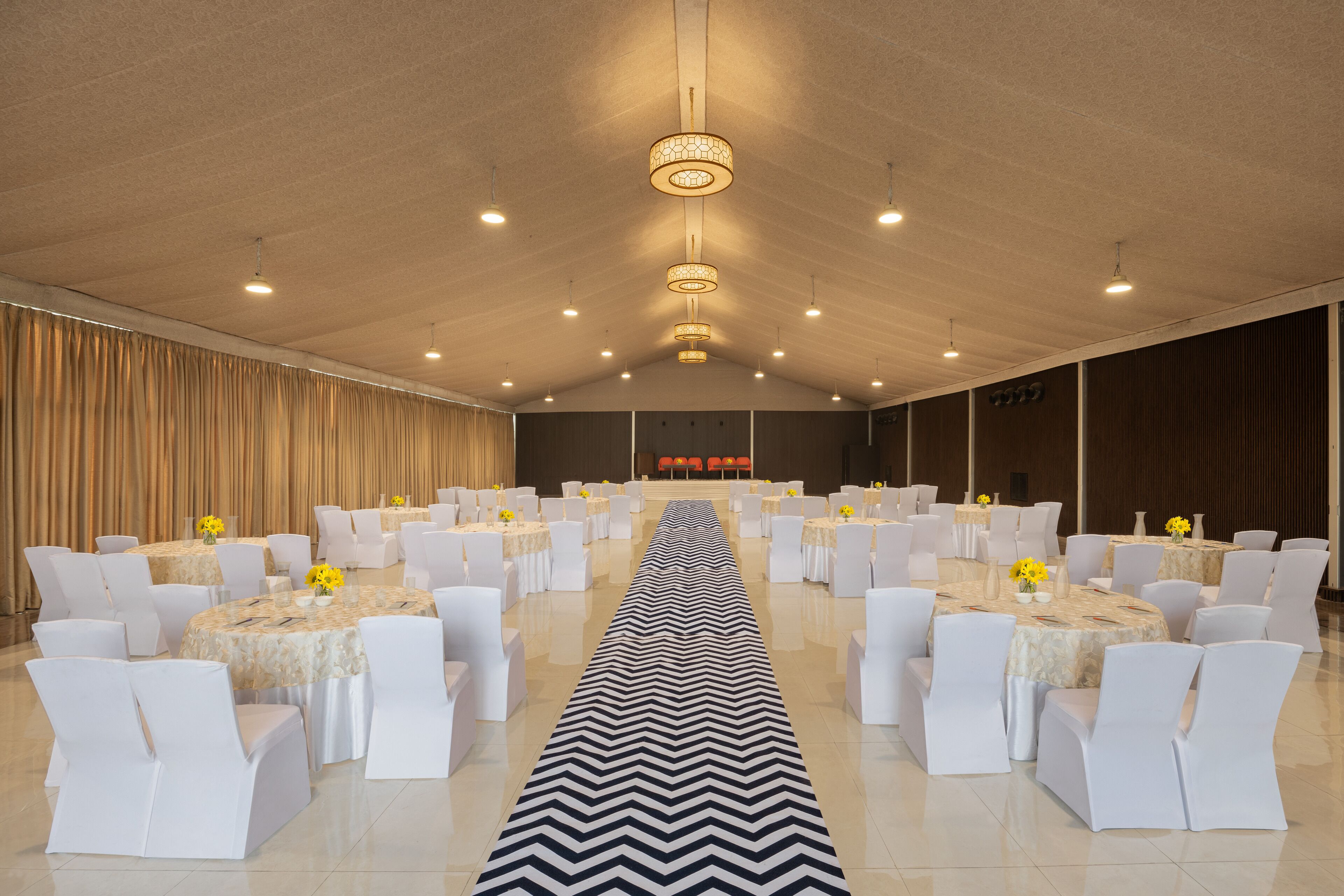 Une salle de banquet avec des tables rondes, des chaises blanches et une allée centrale.