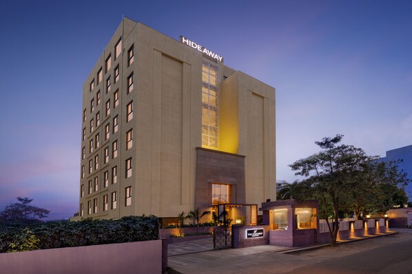 Un hôtel moderne, doté d'une enseigne indiquant « Refuge discret », qui se distingue par son vaste hall d'entrée à la façade vitrée, son éclairage extérieur soigné et son jardin aménagé.