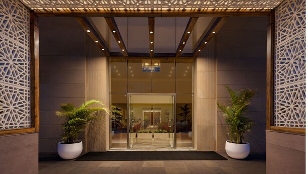 A modern entrance with a glass door, wooden ceiling, and decorative panels. - Ginger Greater Noida Pari Chowk (Greater Noida)