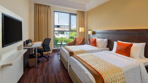 A hotel room with two beds, a desk, a chair, a TV, and a window with curtains. - Ginger Greater Noida Pari Chowk (Greater Noida)