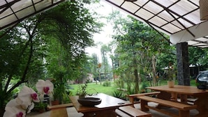 An outdoor patio with wooden tables and benches, surrounded by lush greenery and trees. - Ronia Mountain Villa Lembang (Lembang)