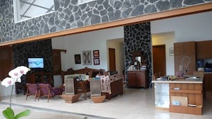 A spacious living area with a stone wall, a television, a dining table, and a kitchen area. - Ronia Mountain Villa Lembang (Lembang)