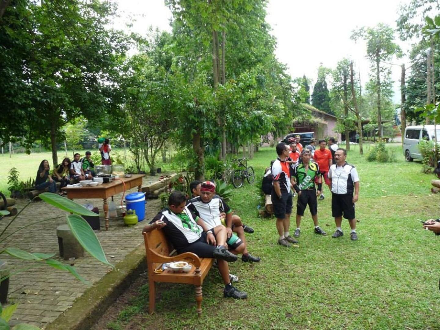 Un grupo de personas reunidas al aire libre, algunas sentadas y otras de pie, con una mesa y sillas cerca.