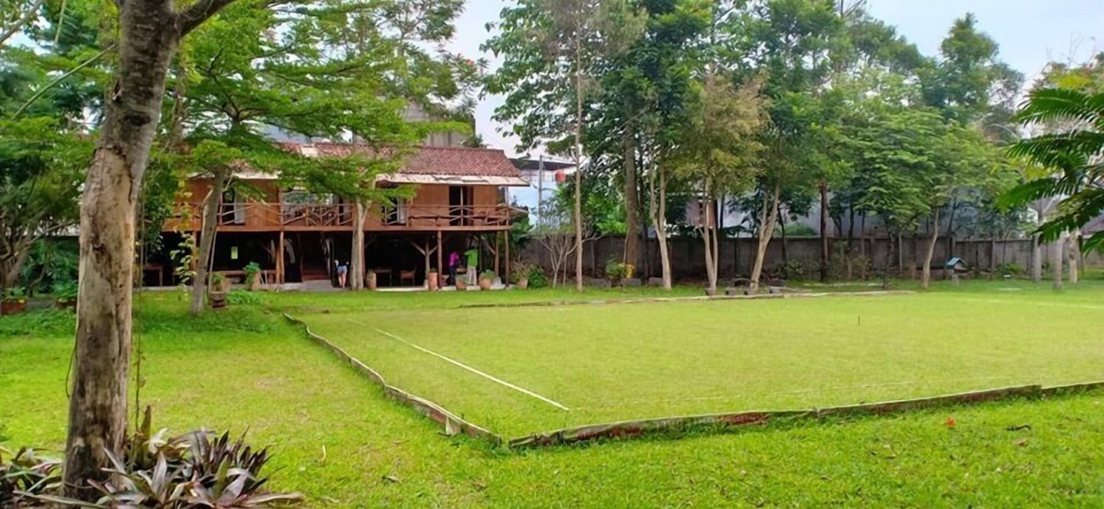 A grassy area with a wooden structure, possibly a house or a pavilion, surrounded by trees.