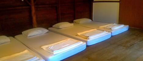 A row of four neatly made beds with white linens, arranged in a room with wooden walls and a wooden floor.