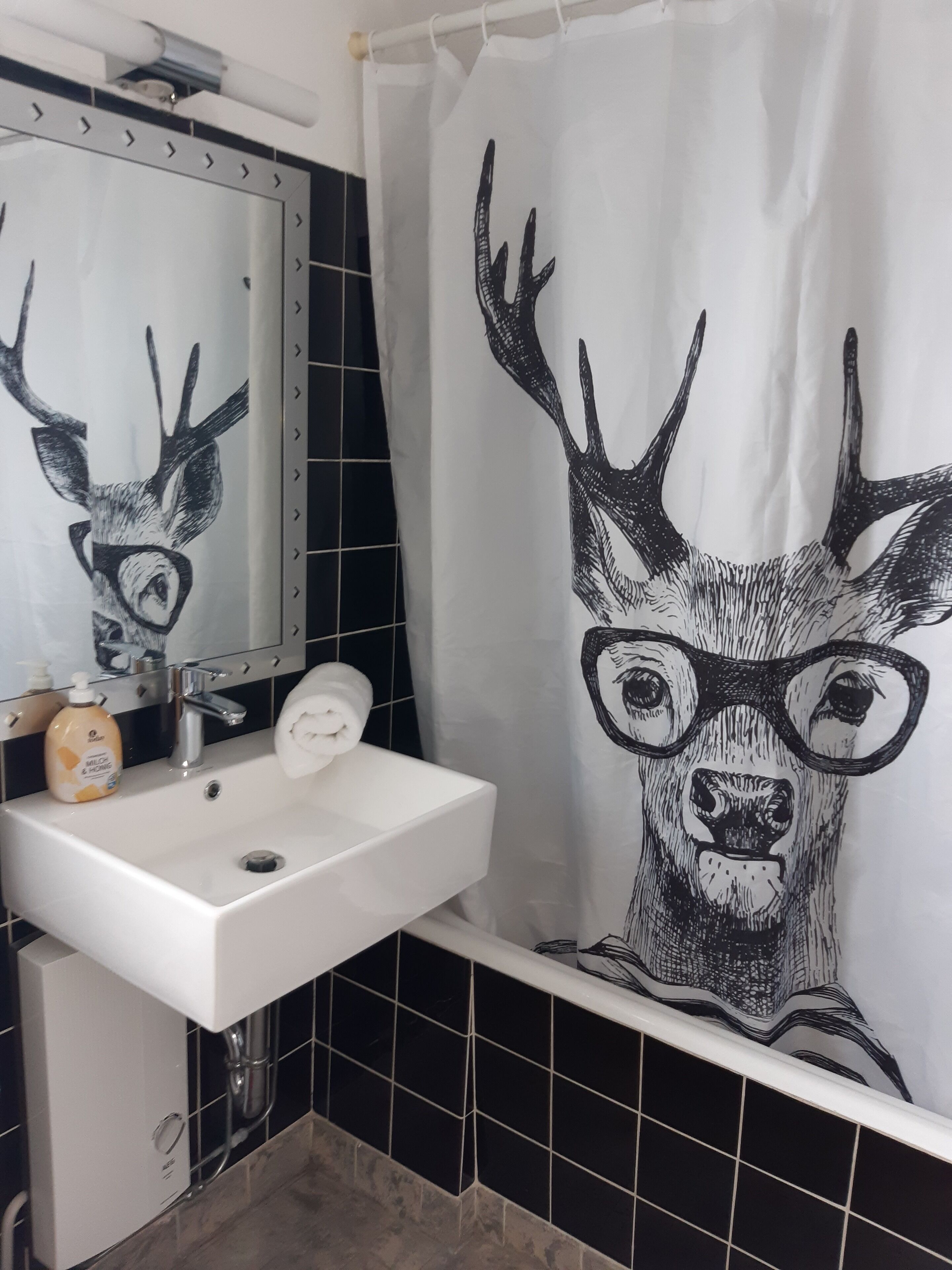 Un baño con lavamanos, espejo y cortina de ducha con una ilustración de ciervo.