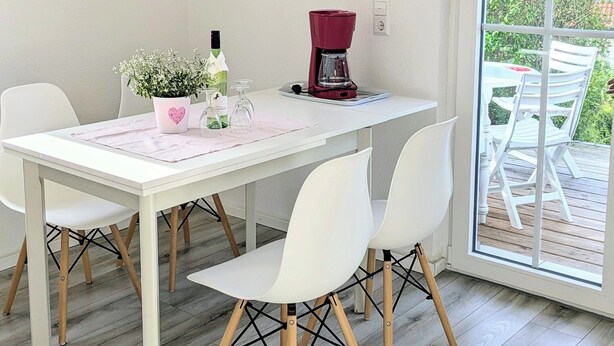 Uma sala de jantar com uma mesa branca, cadeiras brancas, uma luminária pendente e um quadro de uma vaca na parede.