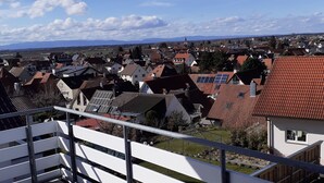 Um deck de madeira com guarda-corpo de metal, com vista para uma área residencial com casas e uma cordilheira ao longe.