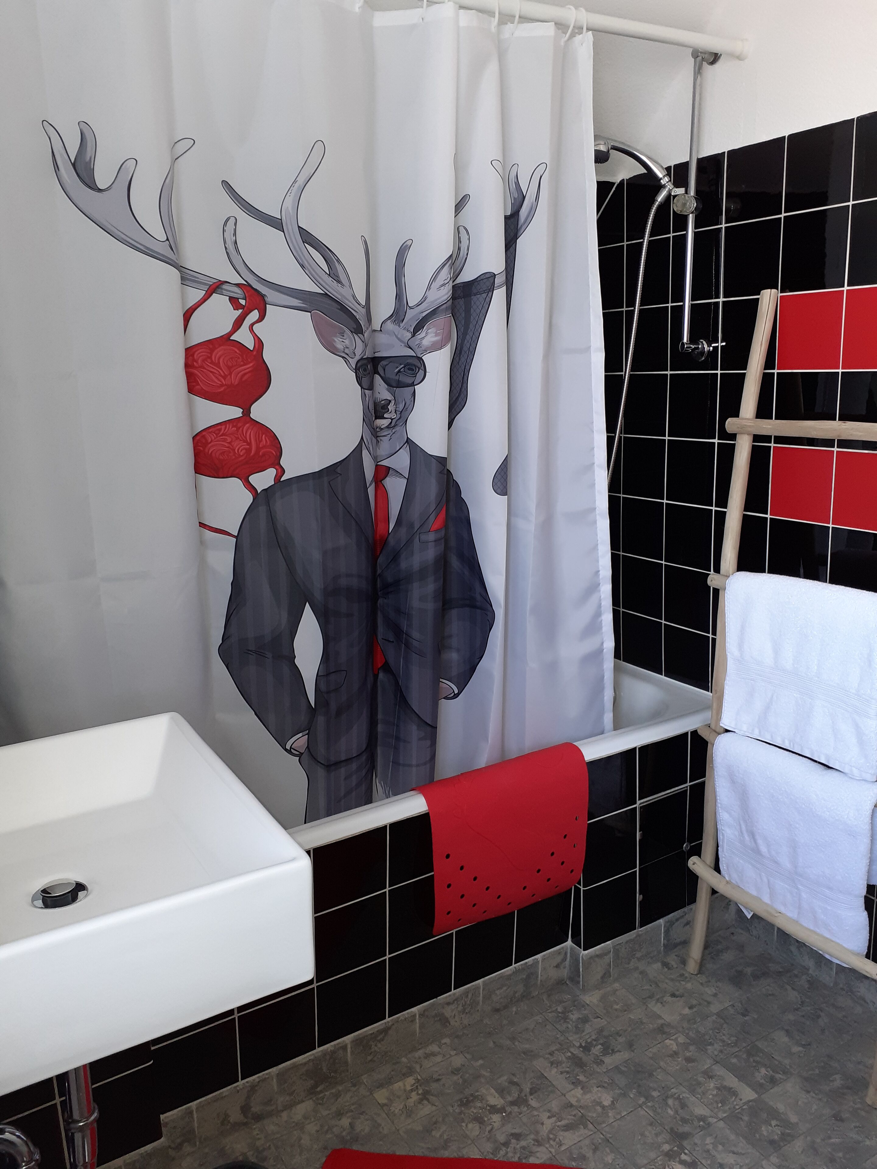 Ein Badezimmer mit Duschvorhang, der eine Hirsch-Illustration zeigt, einem weißen Waschbecken und einem Handtuchhalter mit einem roten Handtuch.