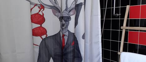Ein Badezimmer mit Duschvorhang, der eine Hirsch-Illustration zeigt, einem weißen Waschbecken und einem Handtuchhalter mit einem roten Handtuch.