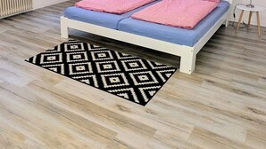 Quarto com cama, mesa de cabeceira, luminária, radiador, estante com livros e um quadro na parede.