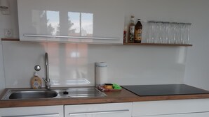 Cozinha moderna com pia de aço inoxidável, bancada de madeira, armários brancos e piso de madeira.