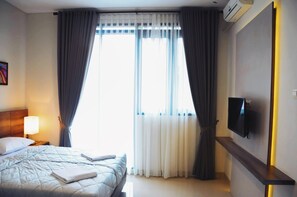 A hotel room with a bed, a bedside lamp, a flat-screen TV mounted on the wall, and a window with curtains. - Rumah Mutiara (Bandung)