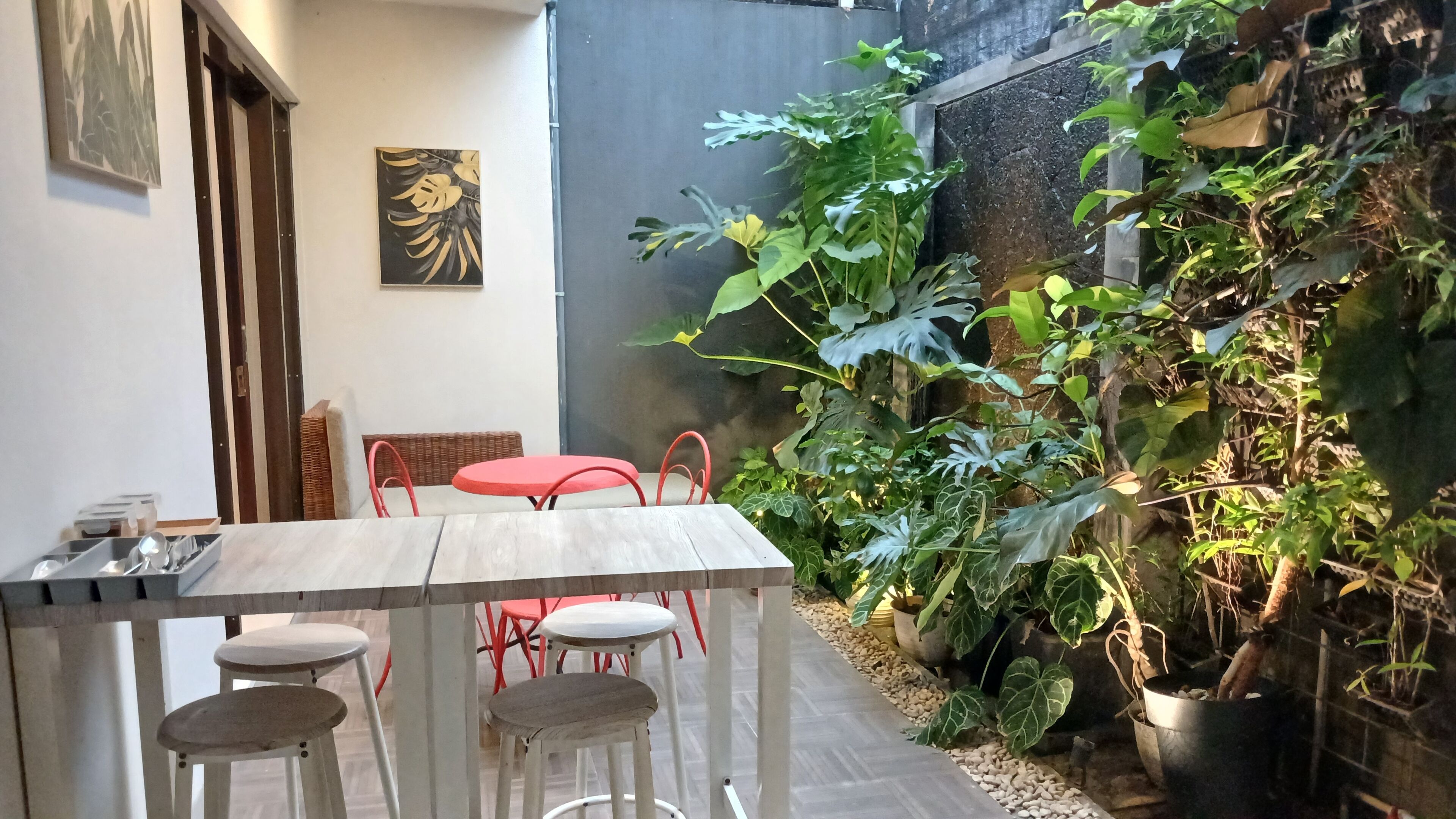 Un comedor con una mesa y sillas, una silla roja, una silla blanca y una mesa roja. Se observa una pared con un cuadro y una planta en maceta.