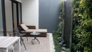 A modern outdoor seating area with a wicker sofa, a small round table, and a metal chair. - Rumah Mutiara (Bandung)