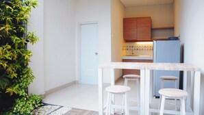 A compact kitchen with wooden cabinets, a white refrigerator, and a bar stool seating area. - Rumah Mutiara (Bandung)