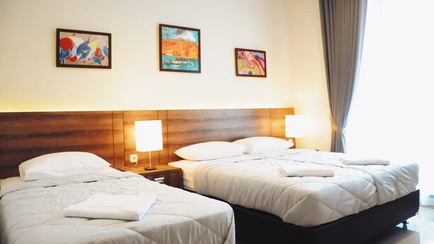 A hotel room with two beds, a wooden headboard, bedside lamps, and three framed artworks on the wall. - Rumah Mutiara (Bandung)