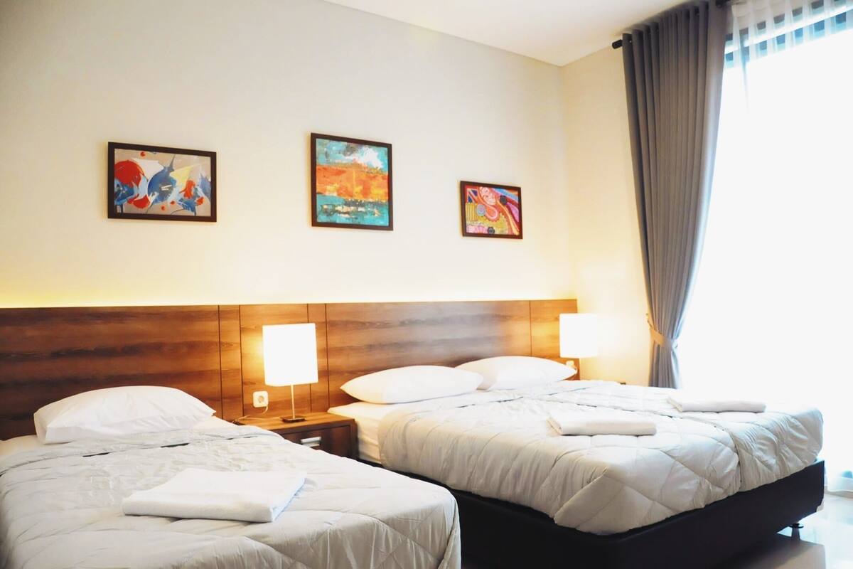 Une chambre d’hôtel avec deux lits, une tête de lit en bois, des lampes de chevet et trois œuvres d’art encadrées accrochées au mur.