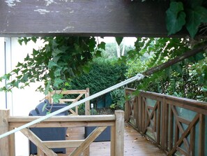 Eine Holzterrasse mit Seilgeländer, einer Sitzgelegenheit und Blick auf viel Grün.
