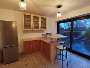 A kitchen with a refrigerator, wooden cabinets, a countertop, and a window with a view of the outside.