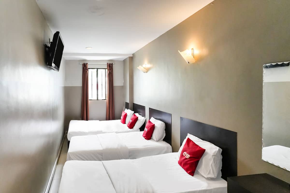 Habitació d'hotel amb tres llits individuals, cadascun amb roba de llit blanca i almoades vermelles, un televisor de pantalla plana penjat a la paret i una finestra amb cortines.