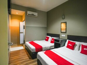A hotel room with two beds, each with red and white bedding, a bedside table, a mirror, and an air conditioning unit on the wall.