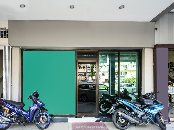 A storefront with a green door and a "WELCOME" mat. Two motorcycles are parked outside.