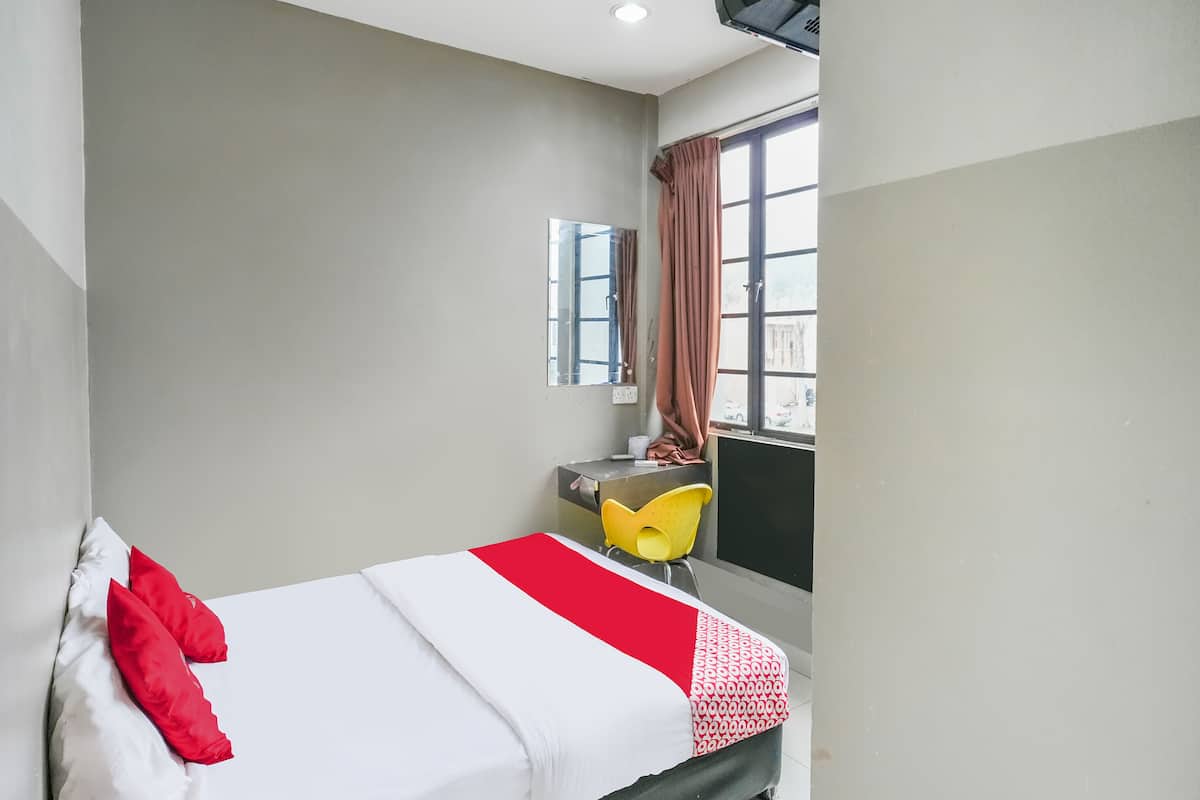 Habitació d'hotel amb llit, escriptori, cadira i finestra amb cortines.