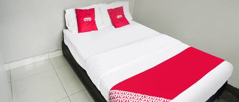 Una cama bien hecha con ropa de cama blanca y roja, incluyendo almohadas con la marca 'OYO'.