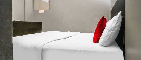 A modern hotel room with a bed, white bedding, a red pillow, and a mirror on the wall.